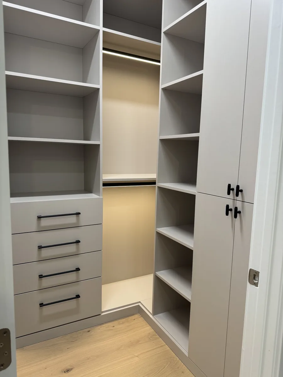 Light grey walk-in closet with hinged doors, open shelves, hanging rail and a drawer bank