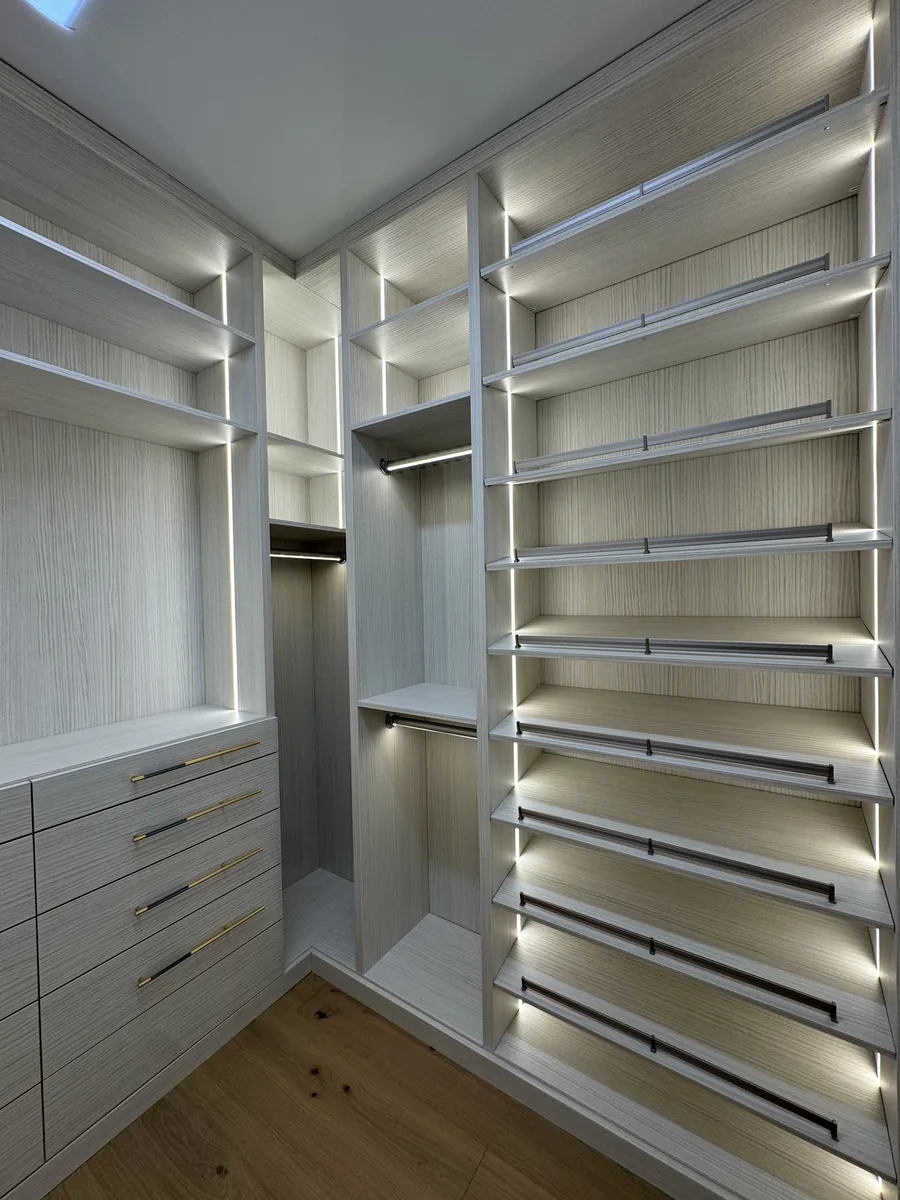 L-shaped walk-in closet in light grey with LED-lit shelves, double hanging and drawer banks