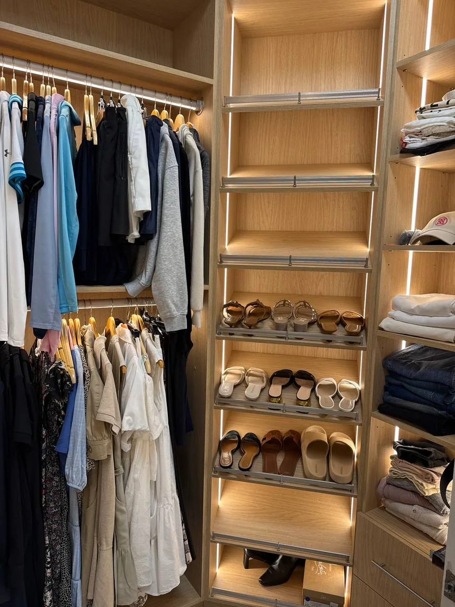 Oak walk-in closet in use: lit shoe shelves, hanging sections and folded clothes on open shelves
