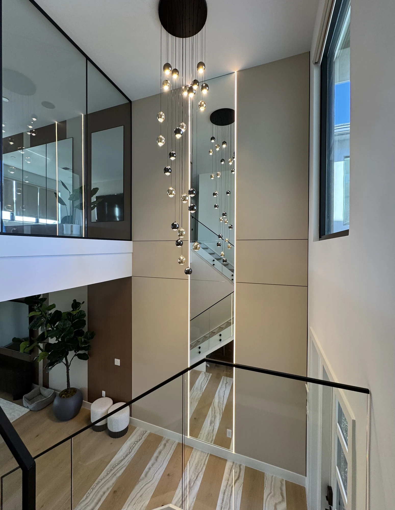 Double-height foyer with cascading pendant lights and mirrored wall panels — interior design by TRE Interiors