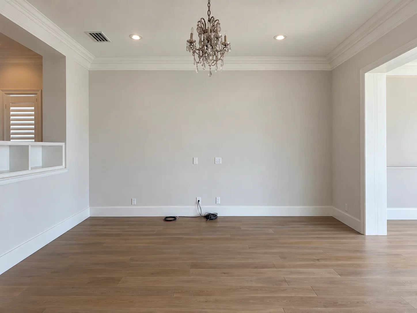 Empty family room with wood floor, crown moulding and a chandelier — before