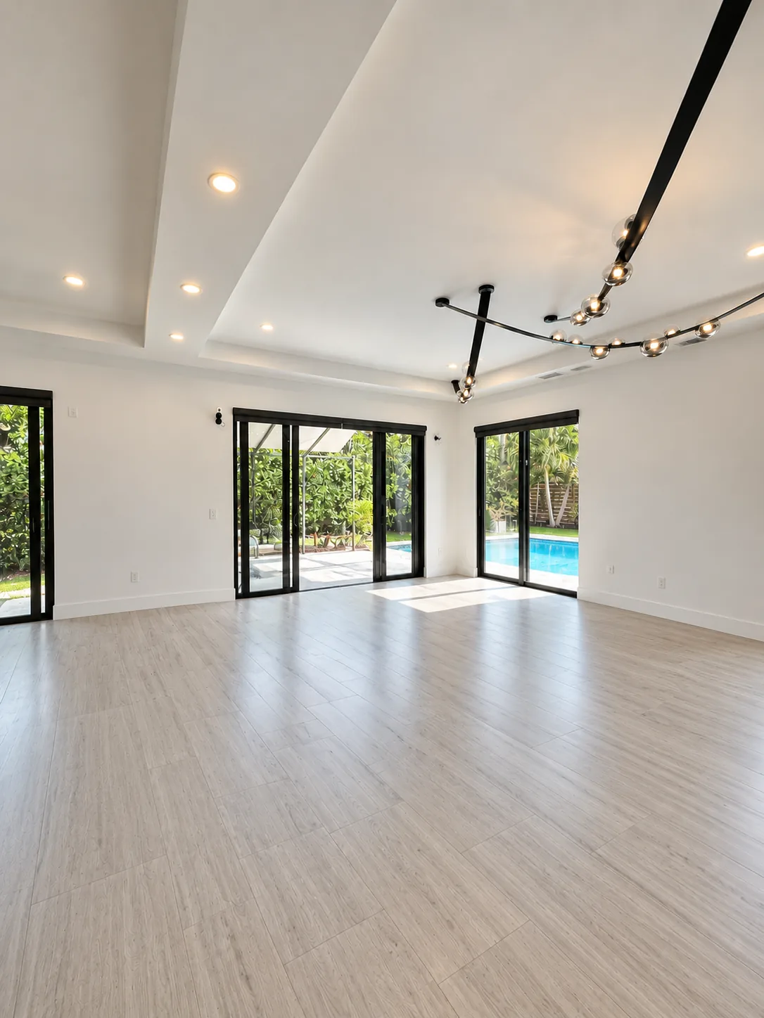 Empty living room with tray ceiling and sliding glass doors to the pool — before