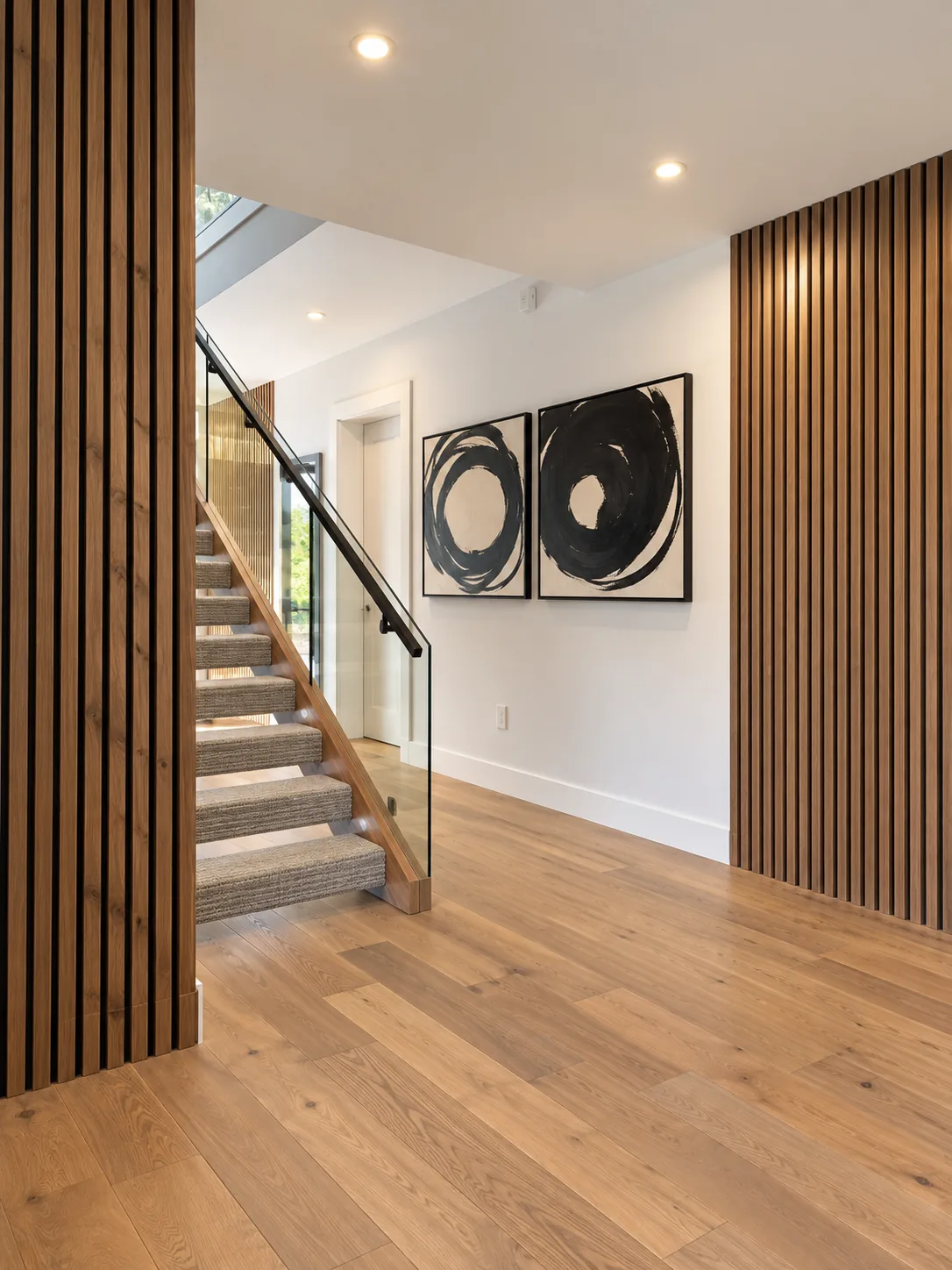 The same foyer with oak slat wall, glass railing and framed art — after