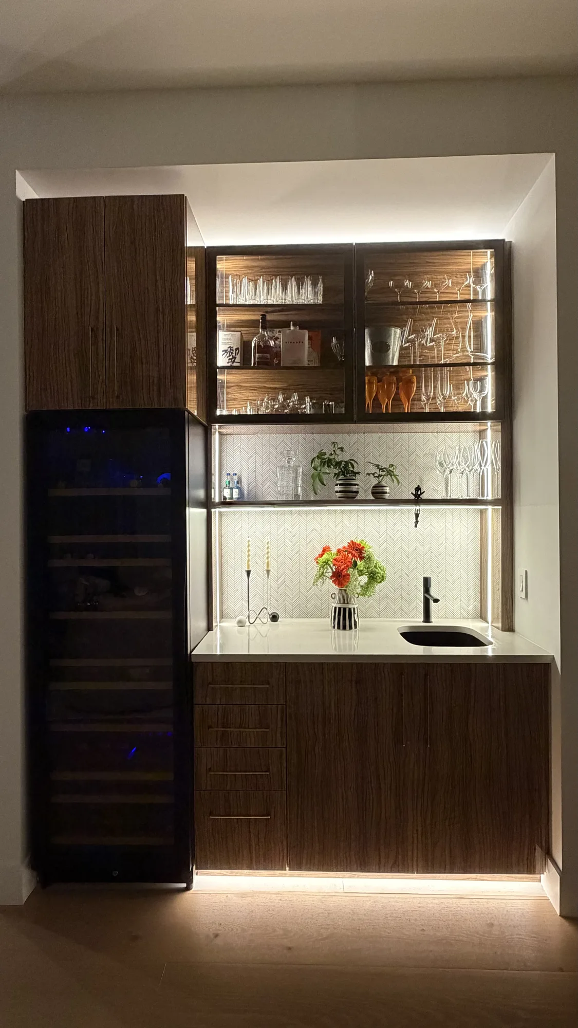 Built-in walnut bar cabinet with wine fridge and lit glass shelves