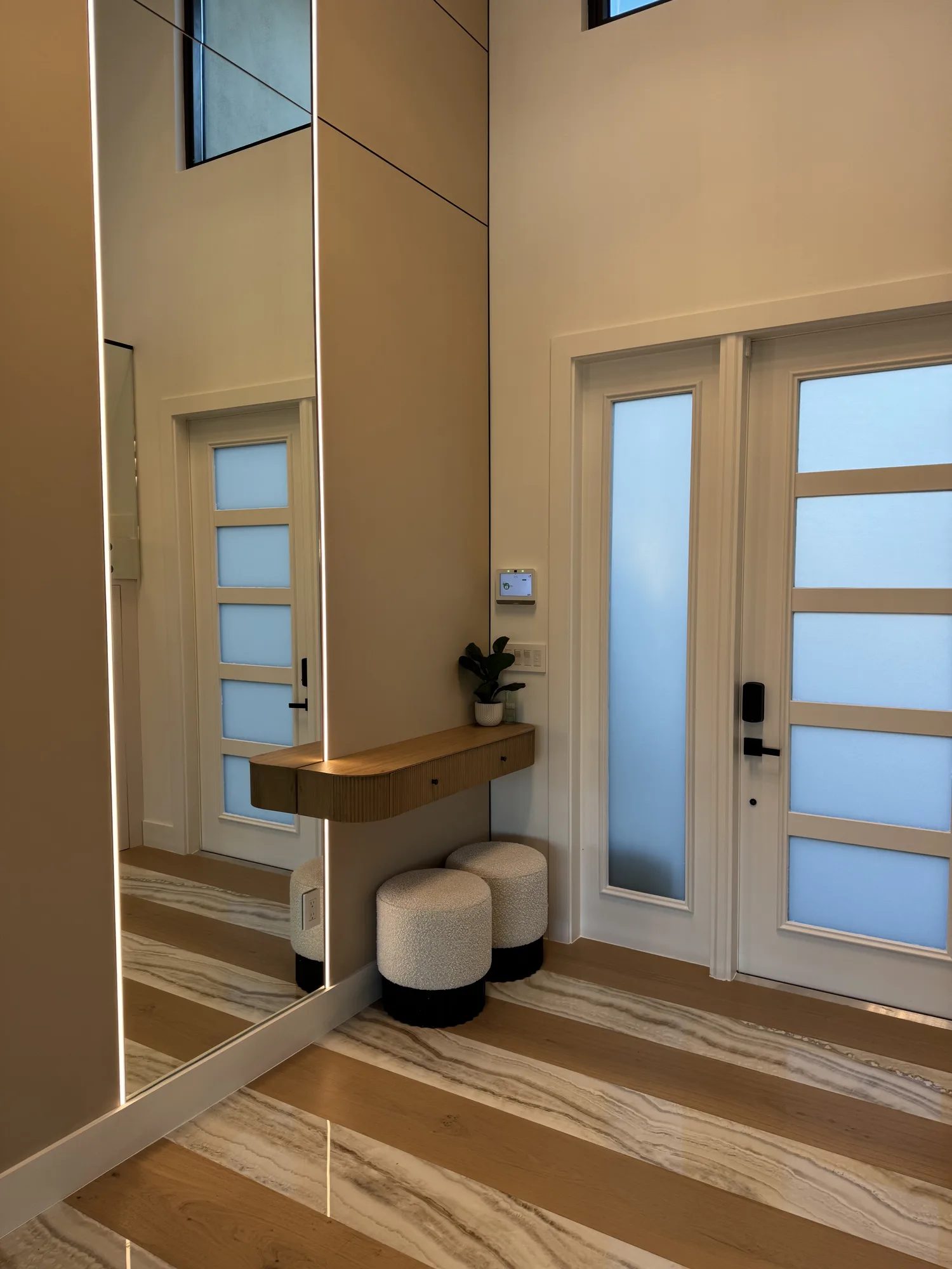 Entry with a floating walnut shelf, full-height wall panels and a mirror