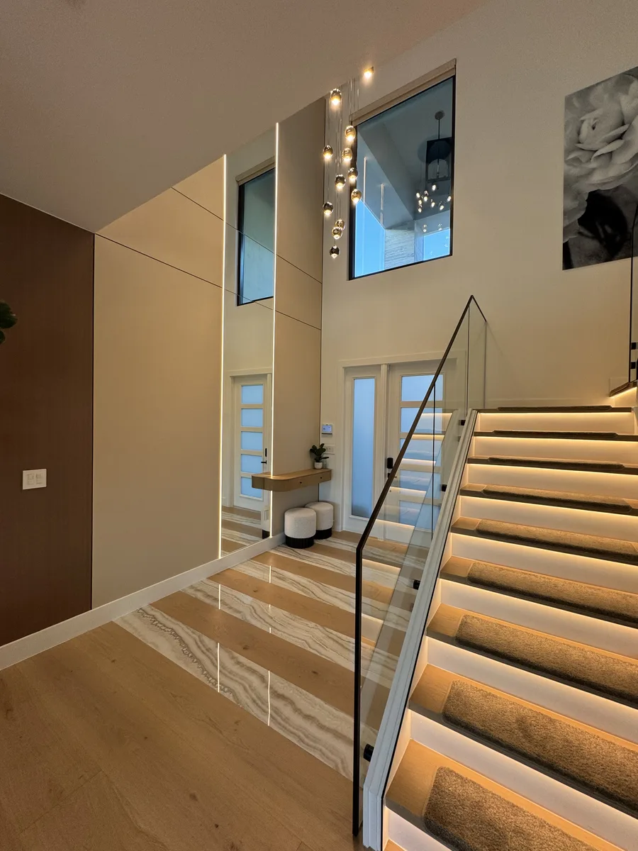 Warm Modern Luxury — foyer with floating staircase, glass railing and backlit steps